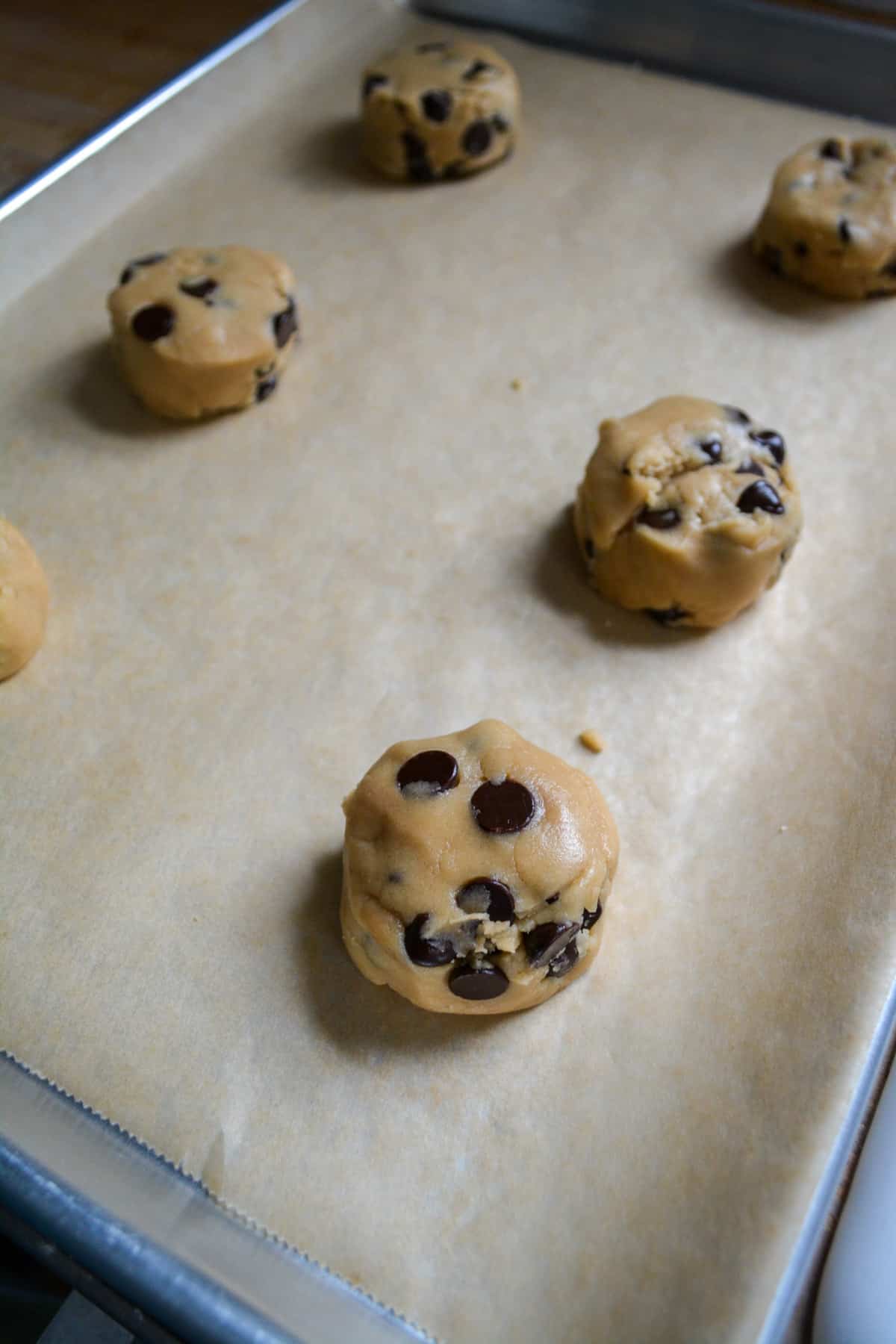 Scooped cookie dough on a parchment lined baking sheet.