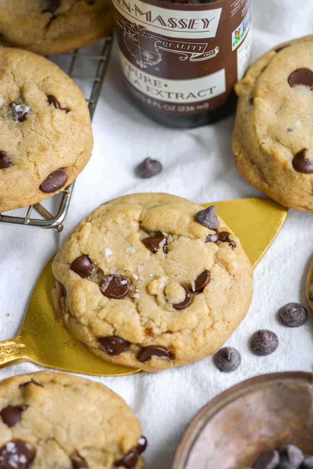 A cookie on a gold cake server with chocolate chips and more cookies in the scene.