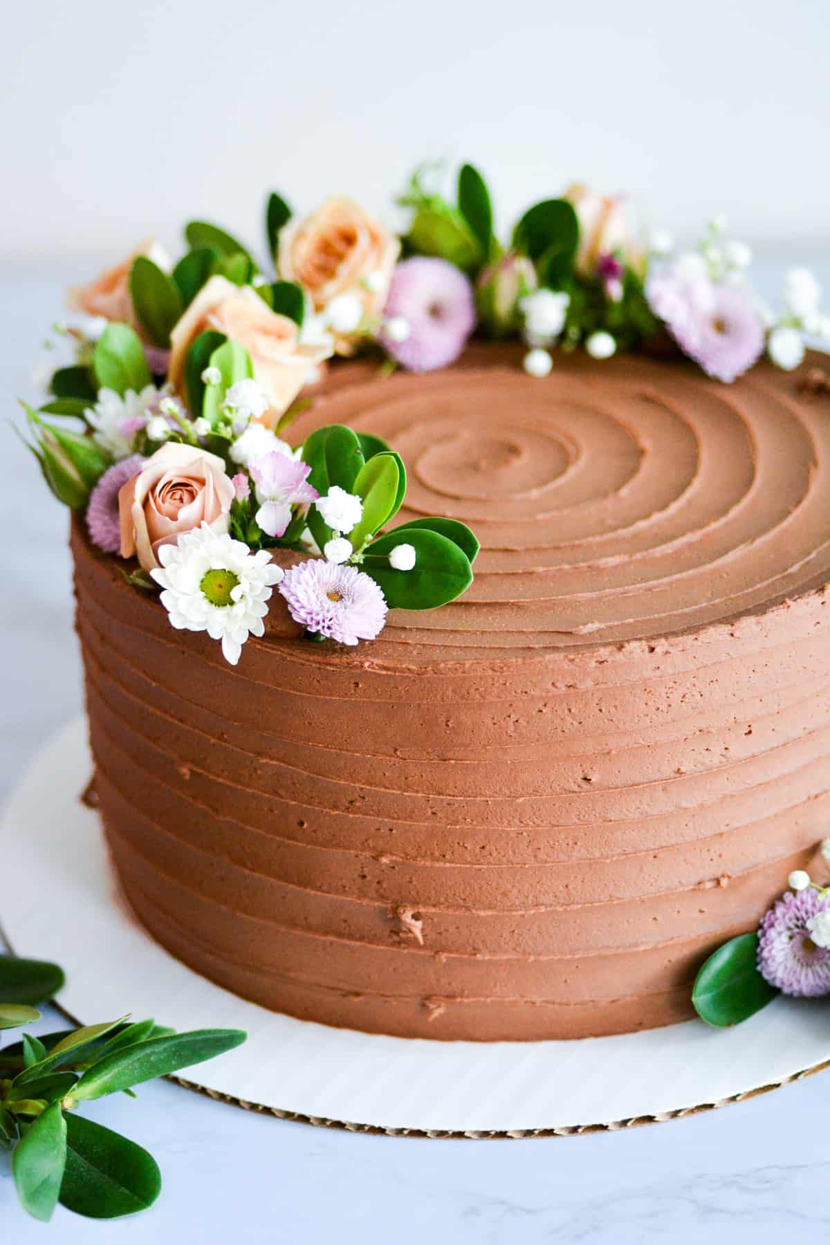 cake frosted with vegan chocolate icing and decorated with purple flowers.