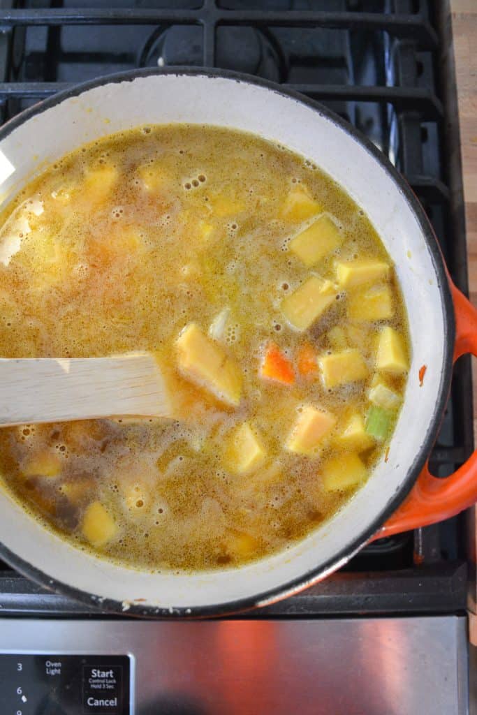 Adding vegetable stock to soup in a pot on the stovetop.