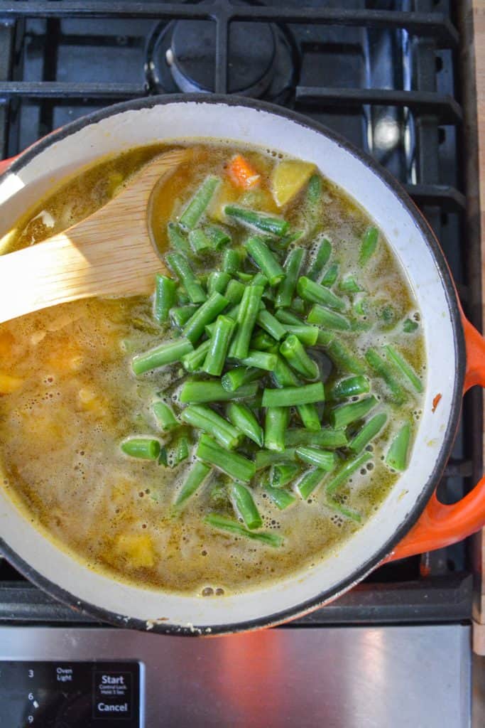 Green beans added to soup in a pot on the stovetop