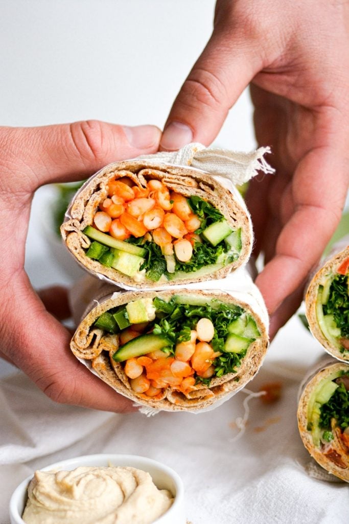 hand holding a pita filled with white bean and tabbouleh