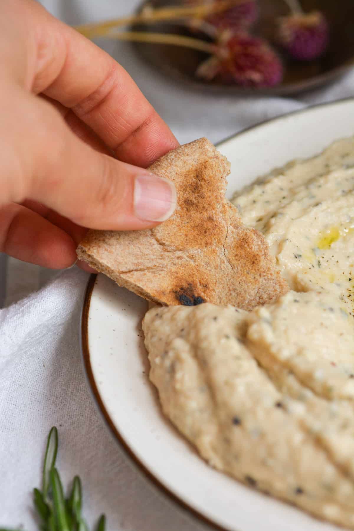 Hand holding pita dipping into the vegan white bean spread