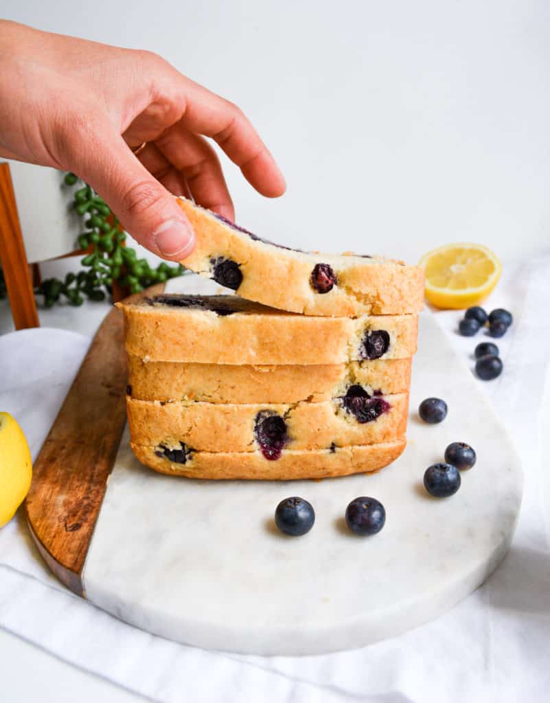 Hand Picking up a slice of stacked One-Bowl Blueberry Lemon Loaf slices
