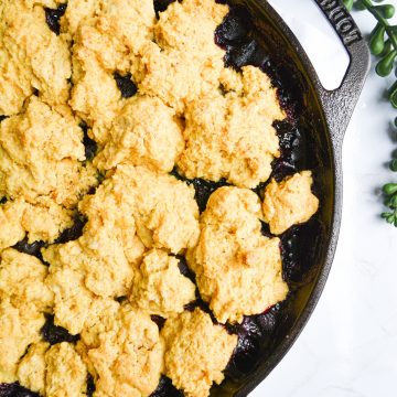 Baked cornmeal biscuit topped berry cobbler in cast iron skillet