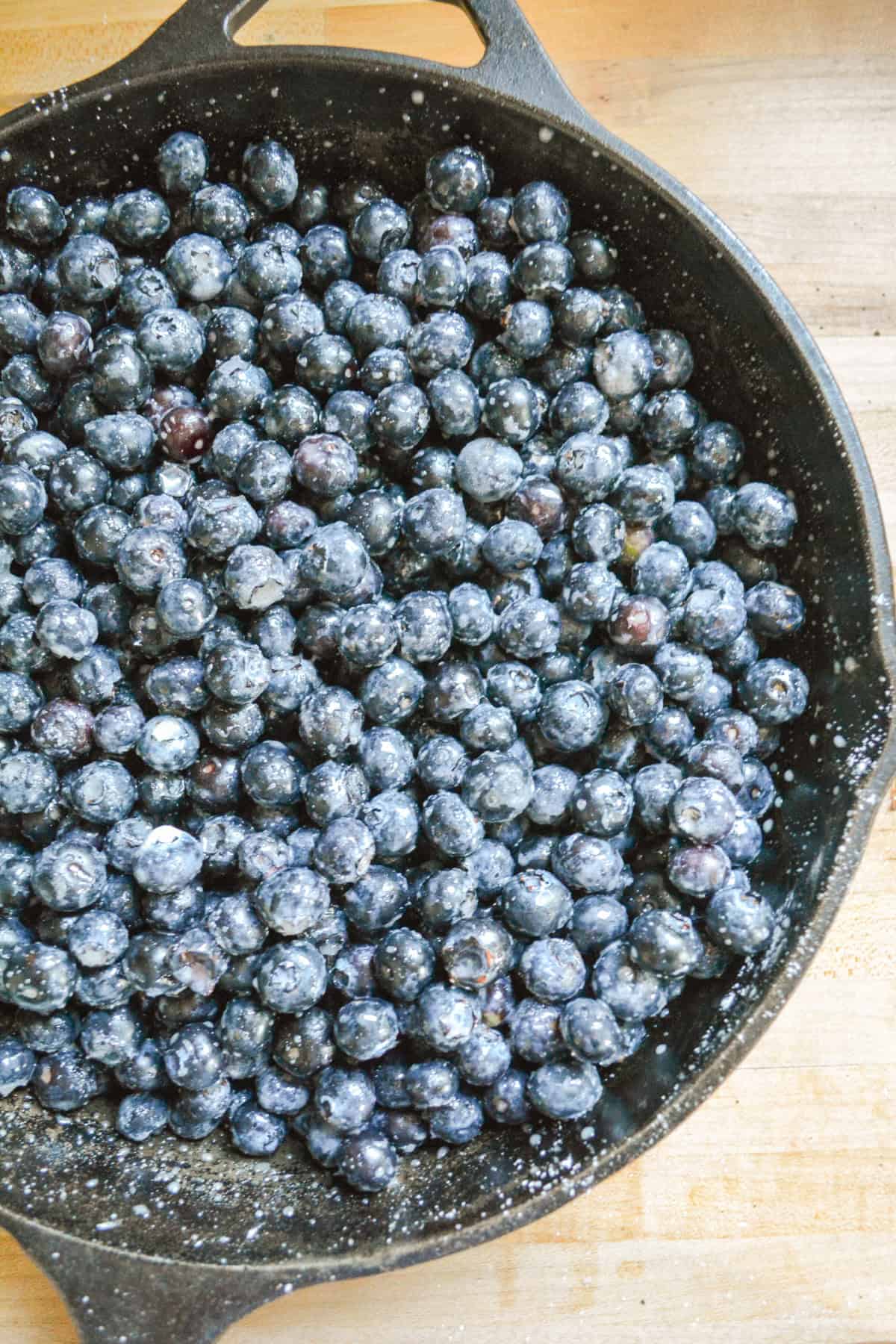 Blueberries all mixed together with sugar and cornstarch in a cast iron skillet.
