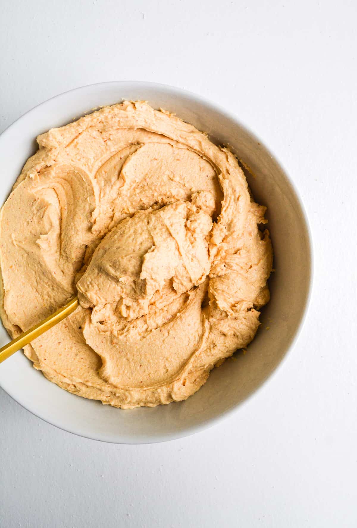 Overhead shot of a bowl of dairy free frosting with a gold spoon inside.