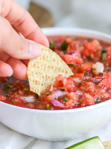 Hand hold a chip dipping into the salsa.