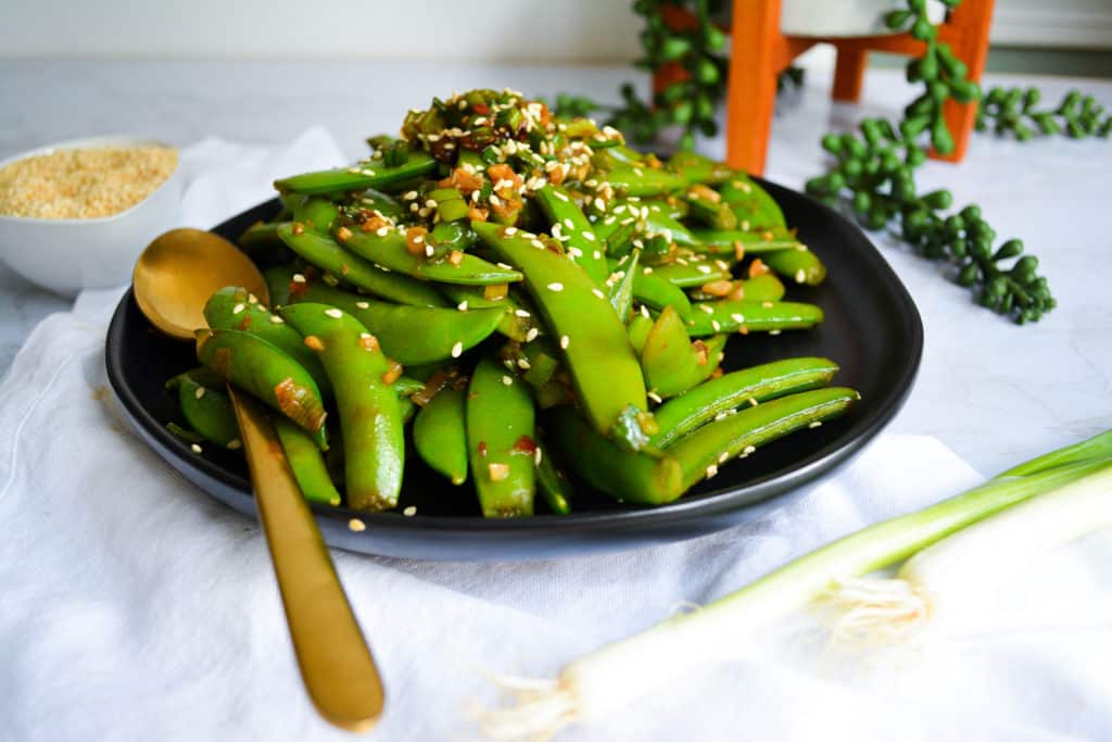Landscape of snap peas on black plate with gold spoon