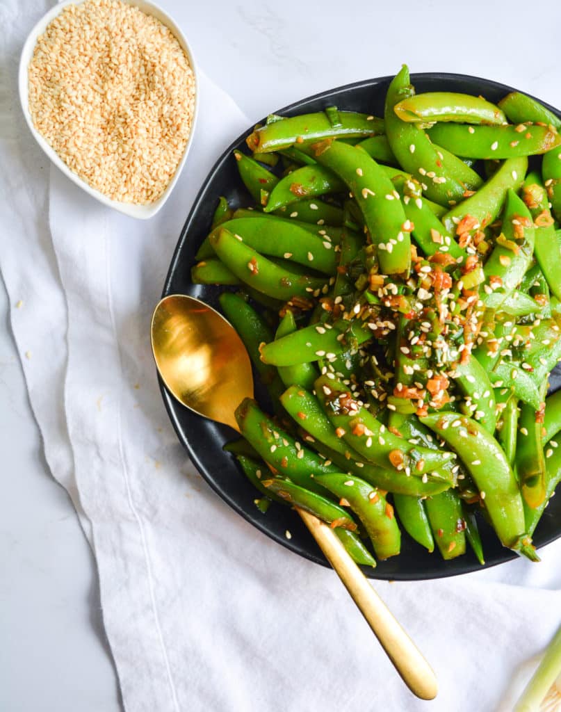 Overhead shot of snap peas on a black plate with toasted sesame seeds