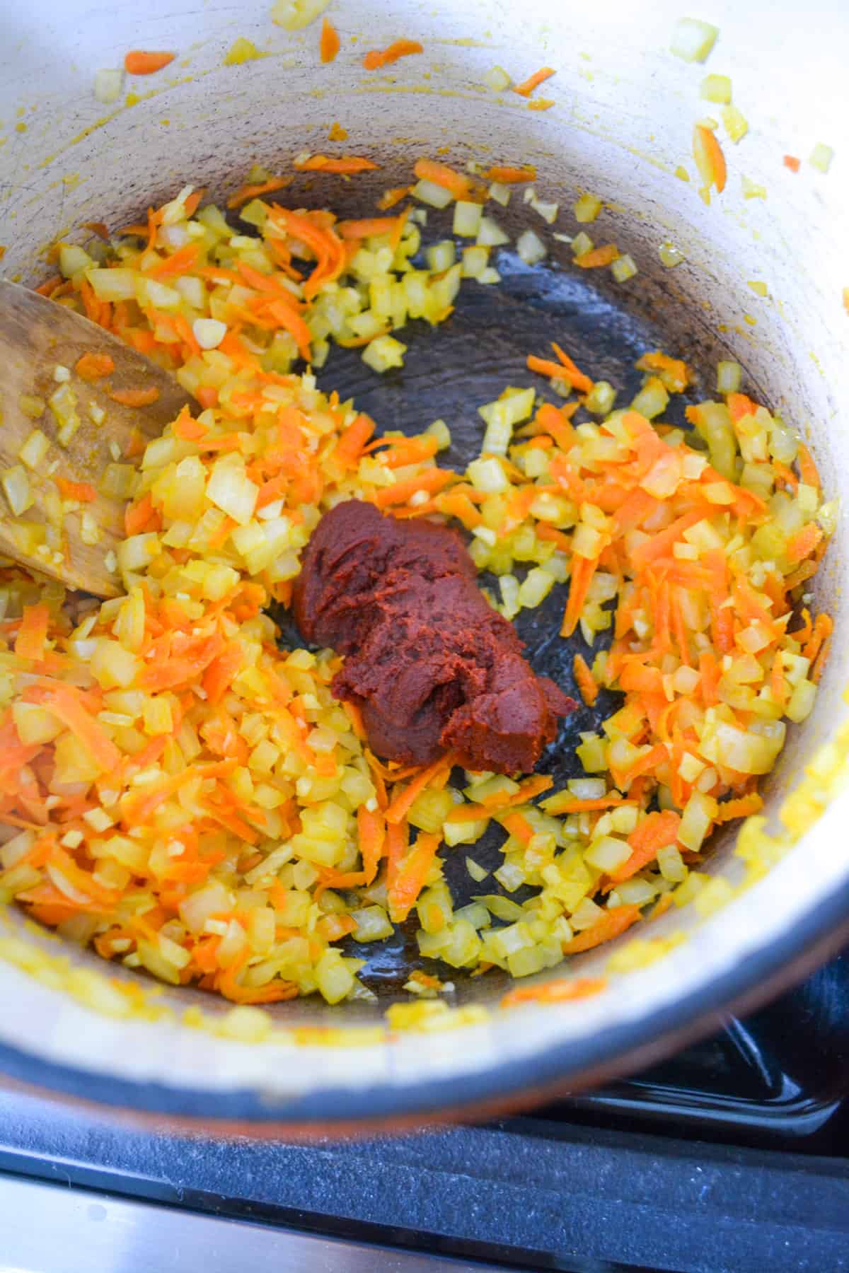 Tomato paste added into the cooking carrots and onion in a pot.