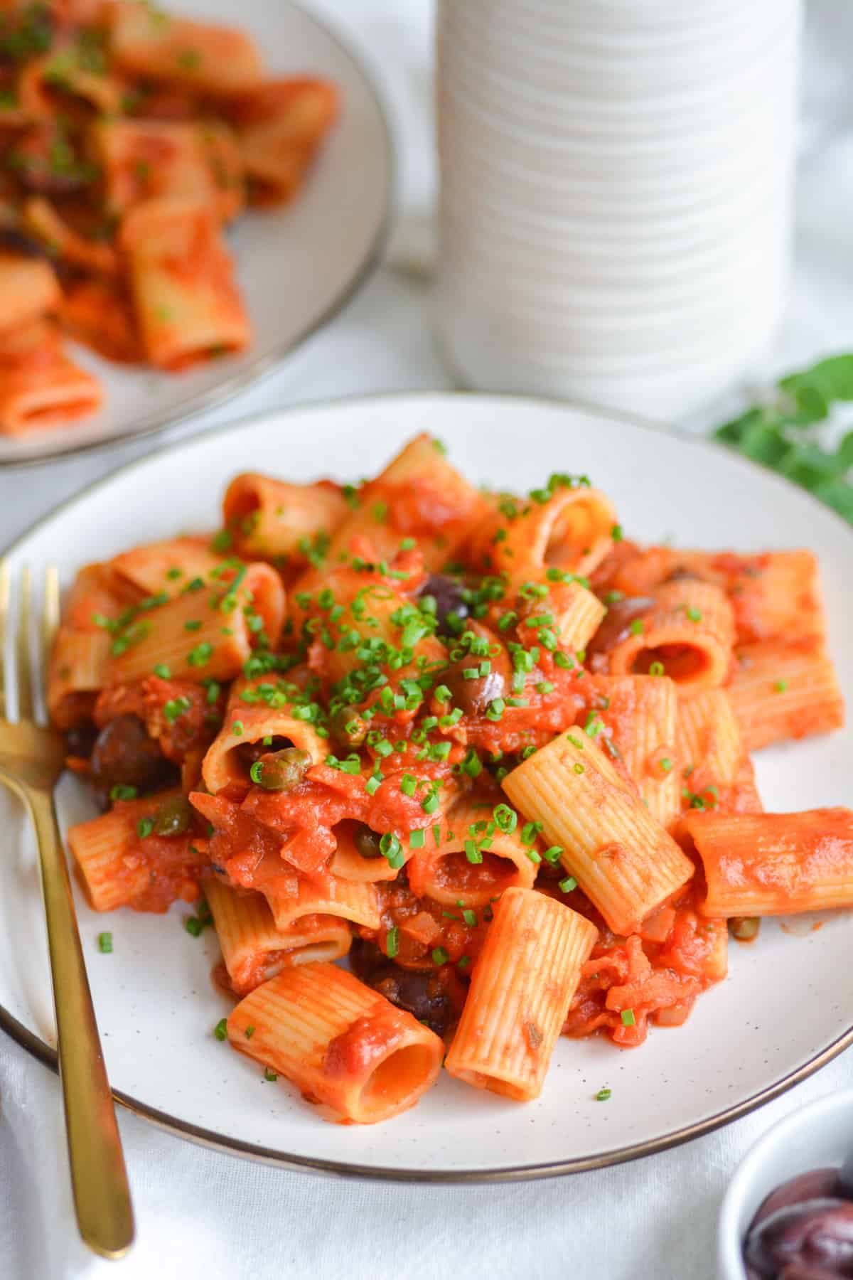 Vegan Puttanesca with rigatoni on a plate with a gold fork to the left side.