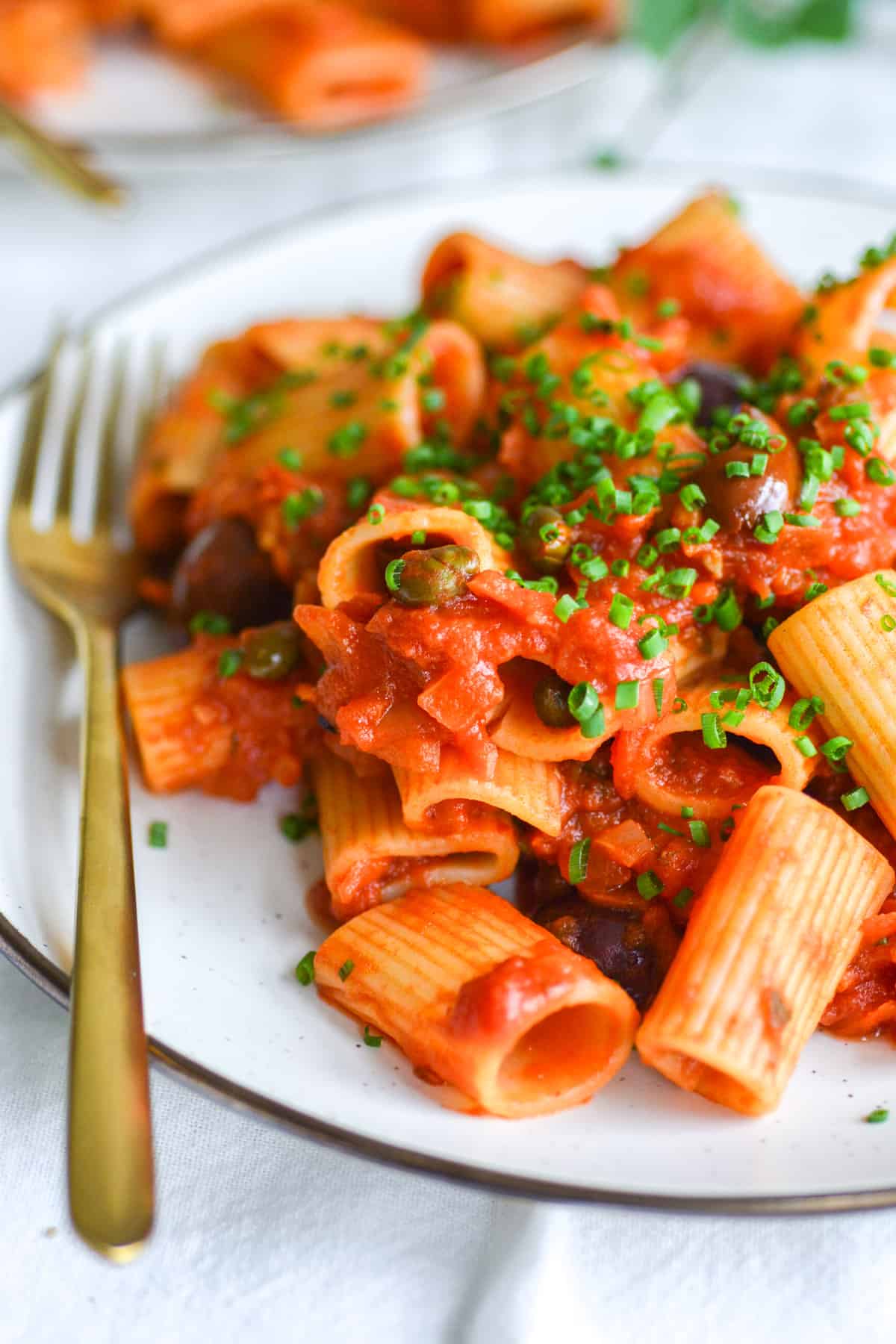 Vegan Pasta Puttanesca with rigatoni on a plate garnished with chives.