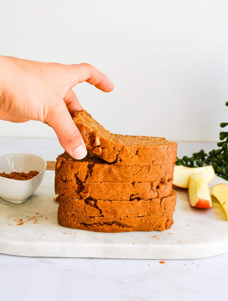 A hand reaching for a slice of Easy Chai Spiced Apple Loaf