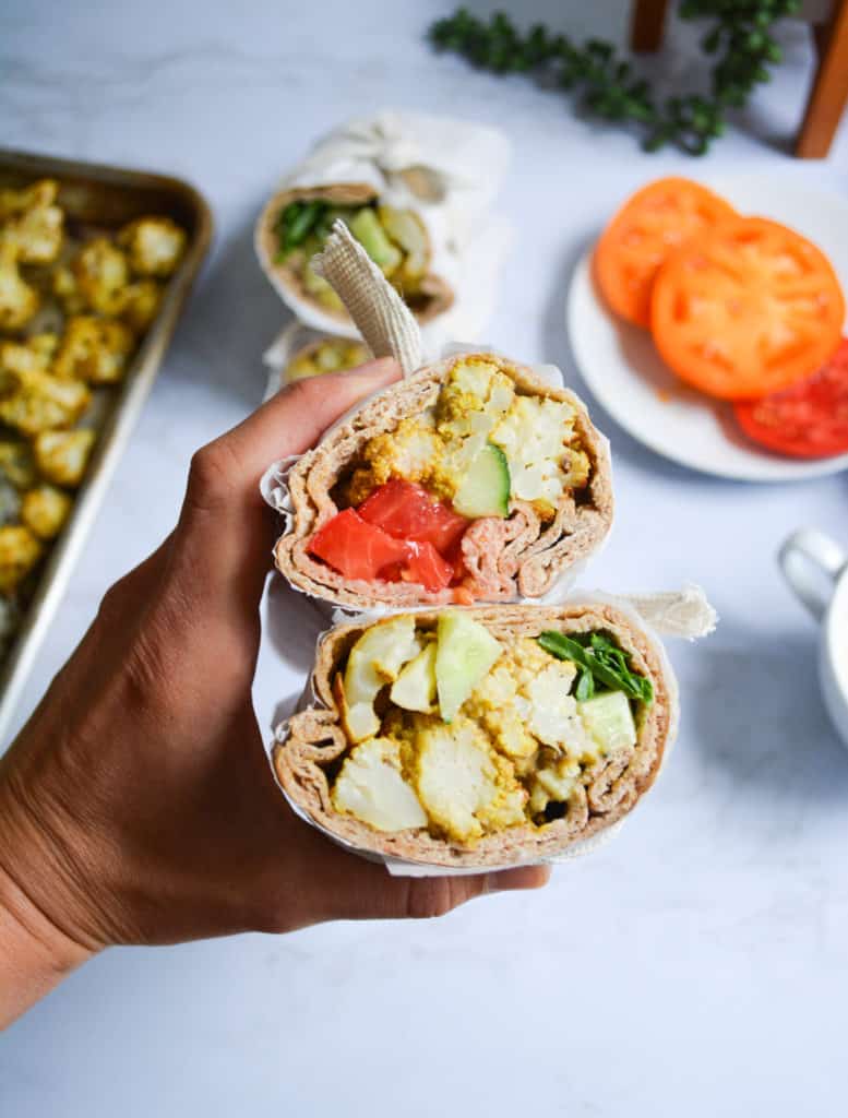 Hand holding a roasted moroccan cauliflower roll up