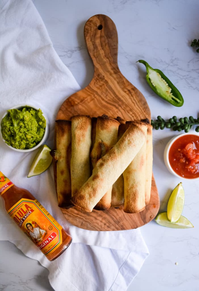 Stacked 30 Minute Chipotle Black Bean taquitos on a wooden board with lime wedges