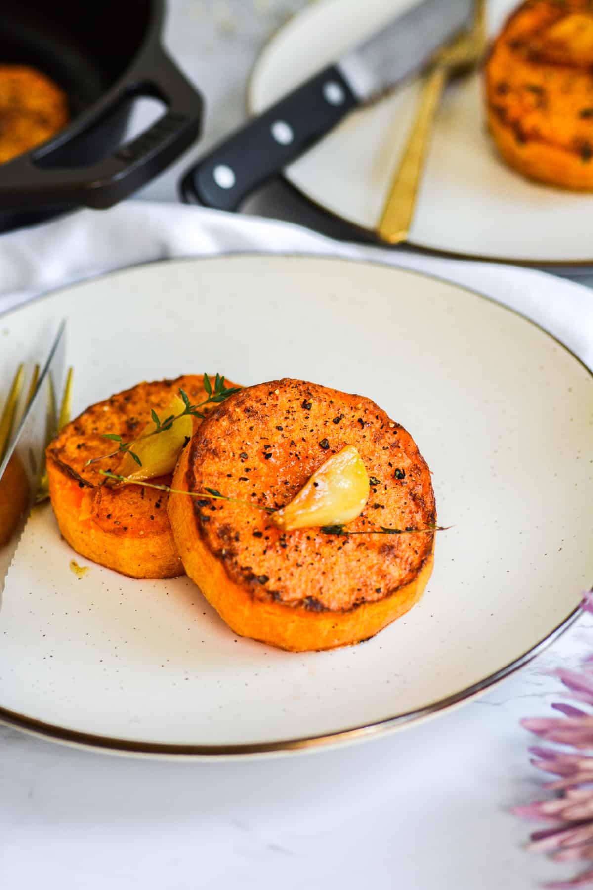 two butternut squash steaks on a plate topped with garlic