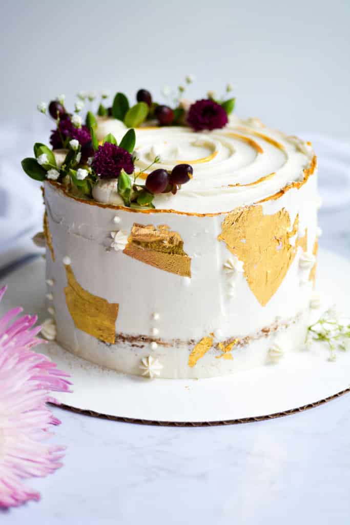 Apple cake decorated with berries, flowers and gold accents