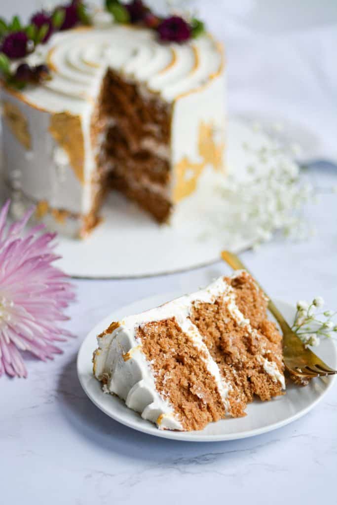 A slice of cake on a white cake with the full cake in the background