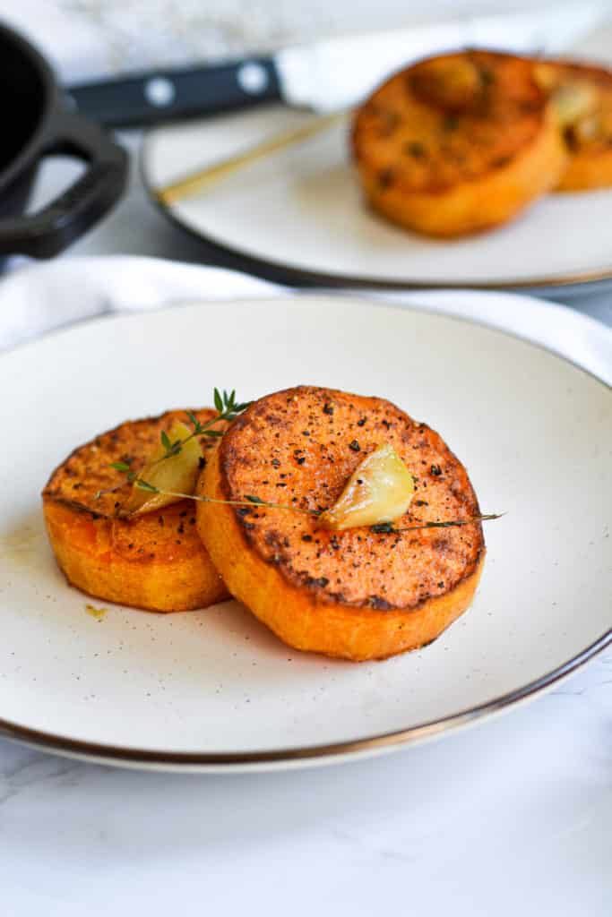 Two Garlig Butter Butternut Squash Steaks topped with toasted garlic and thyme sprigs on a tan plate