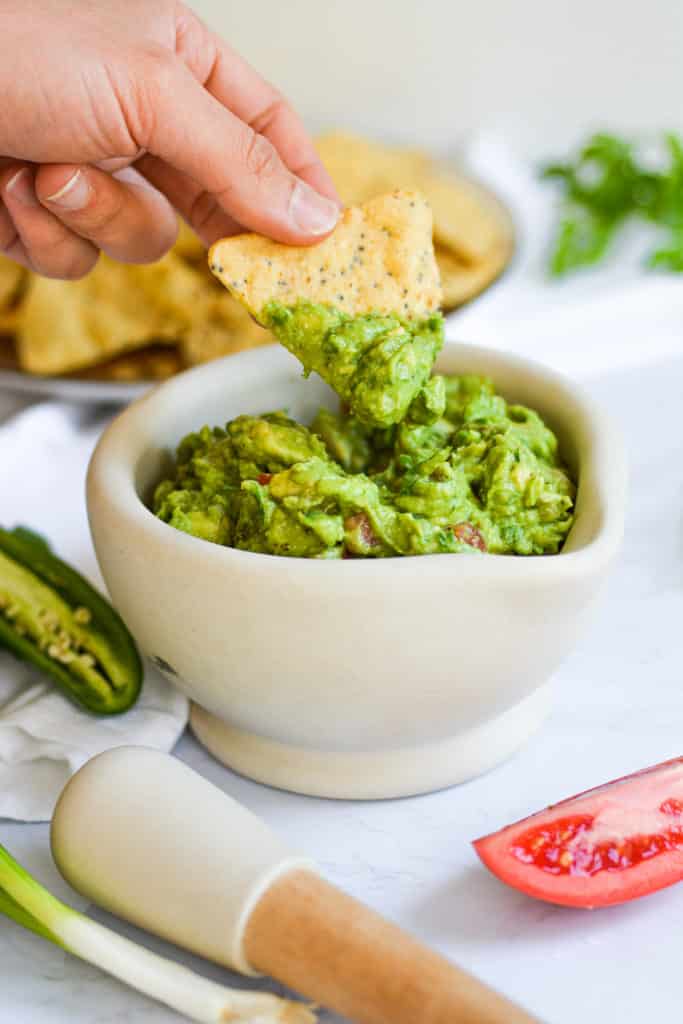 Hand holding a tortilla chip with guacamole on it
