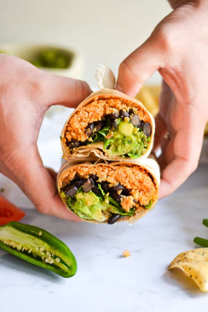 2 hands holding 2 halves of buffalo cauliflower rice burritos with ranch and guac