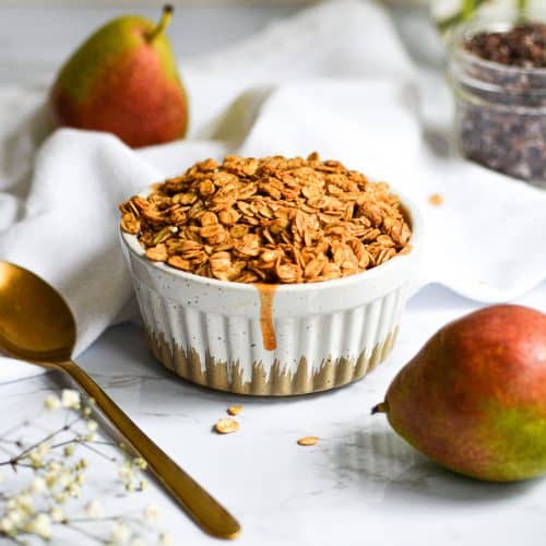 Baked pear crisp in a ramekin with small red and green pears in the background