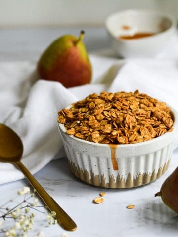 Landscape of a ramekin of Healthy Pear Crisp for one with a flower and small pears in the background