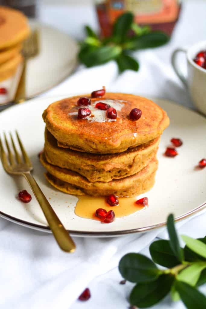 Portrait of a stack of pancakes on a plate with vegan butter, syrup and pomegranate arils