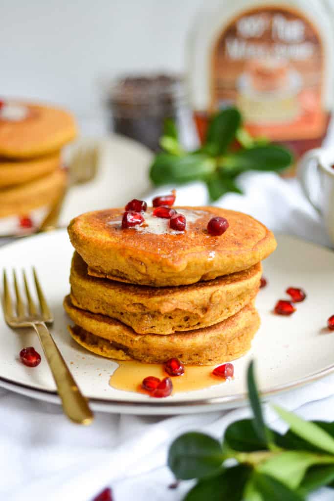 stack of 3 whole grain pumpkin spice pancakes with vegan butter, maple syrup and pomegranate seeds