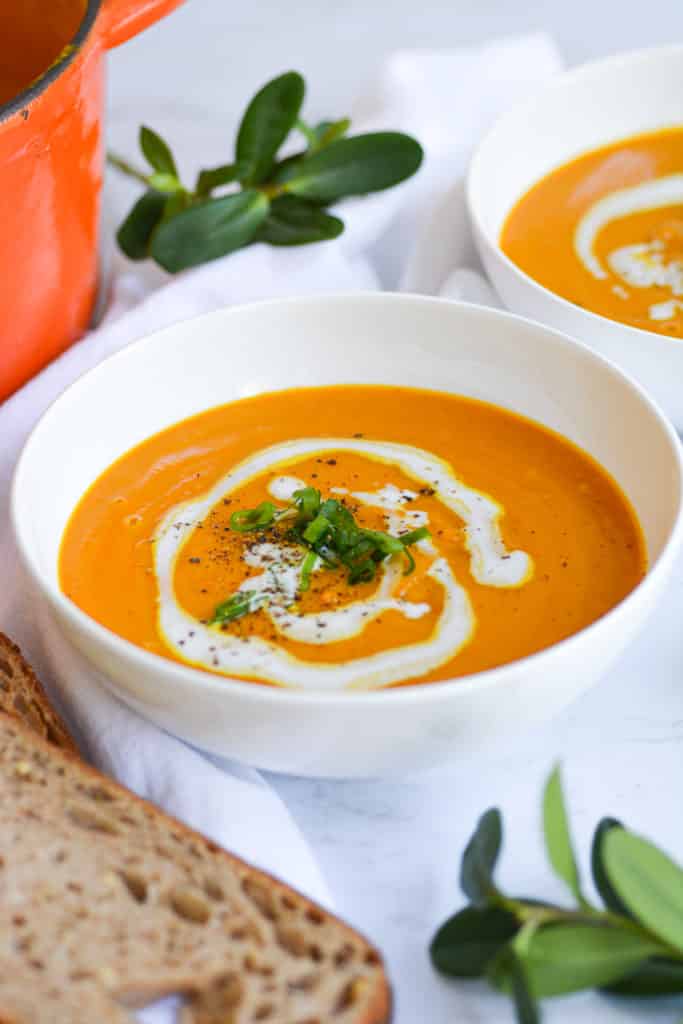 A bowl of Winter Squash Soup, decorated with a drizzle of coconut cream and green onions