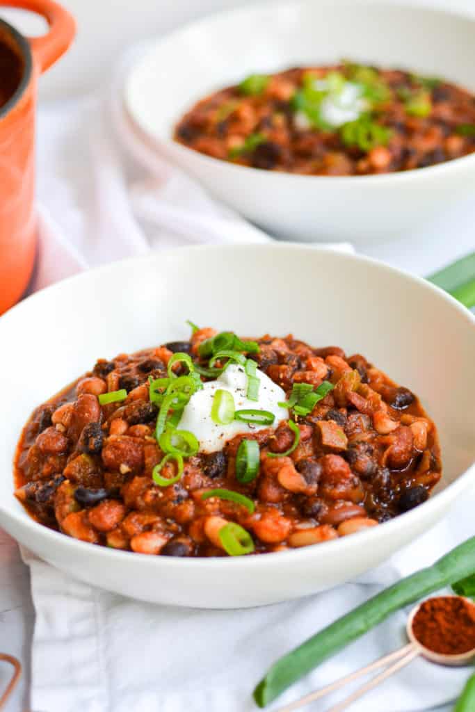 Two bowls of chili in white bowls topped with sour cream and scallions