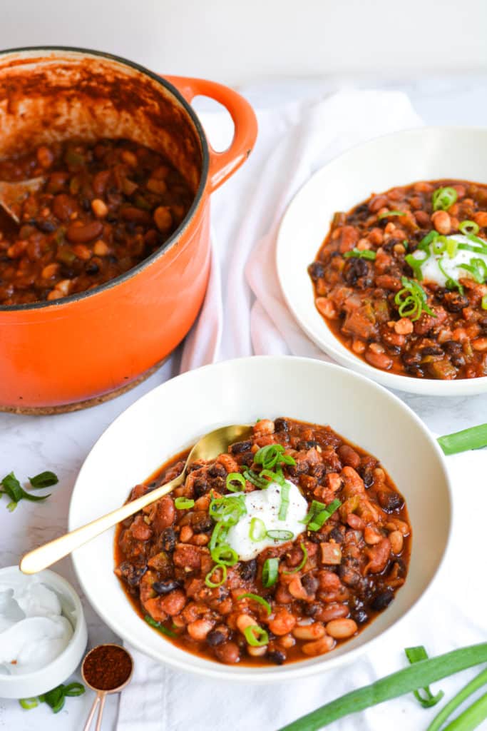 Two bowls of chili topped with sour cream and scallions next to an orange dutch oven