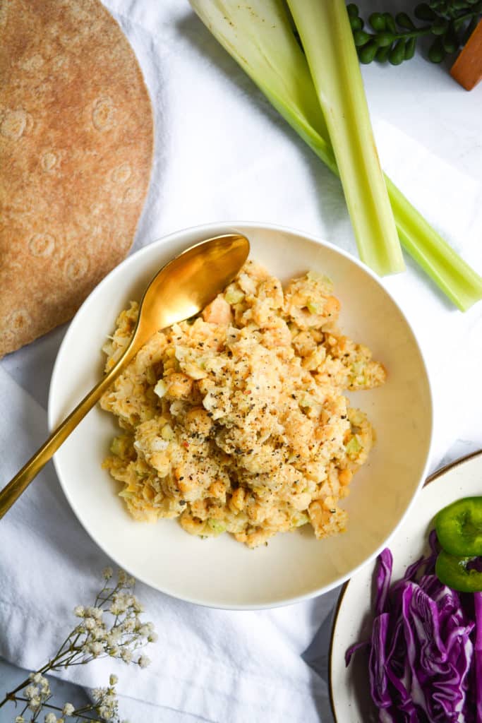 chickpea salad in a white bowl with tortillas and celery in the background