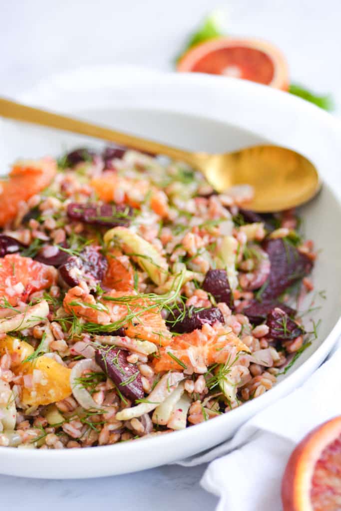 Close up of a bowl of Warm farro salad with a gold serving spoon