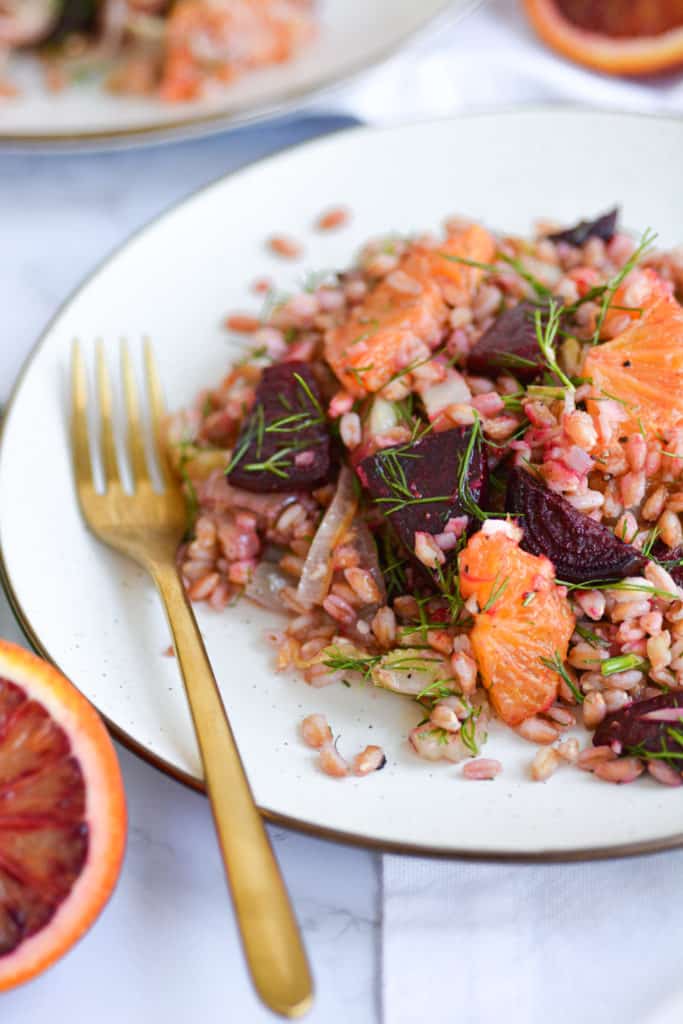 Close up of Warm farro salad on a tan plate with a gold fork