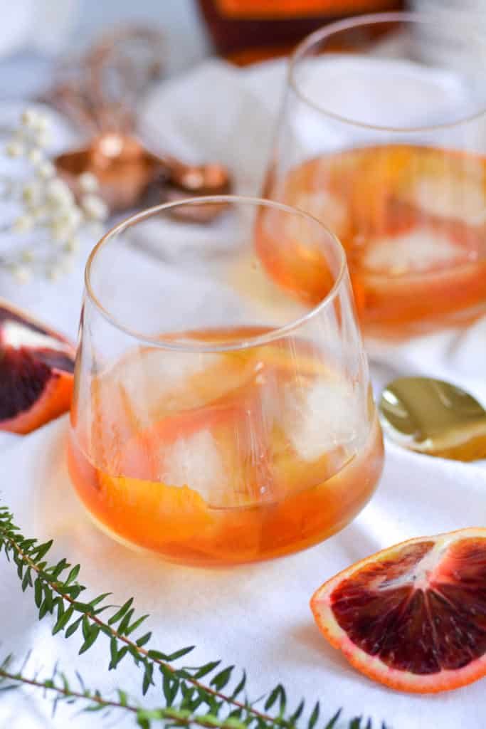 2 glasses of maple bourbon old fashioned on a white background with blood orange slices