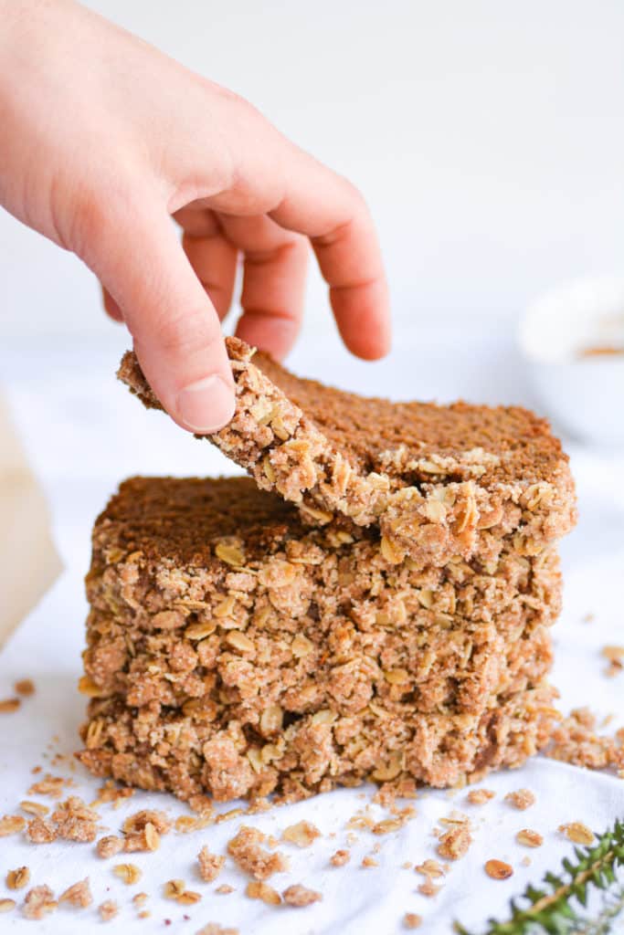 Hand picking up a piece of gingerbread coffee cake from a stack of slices