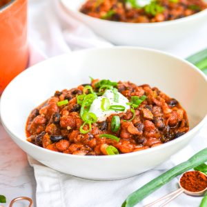 gluten free vegan bean chili in a white bowl with sour cream and green onion on top