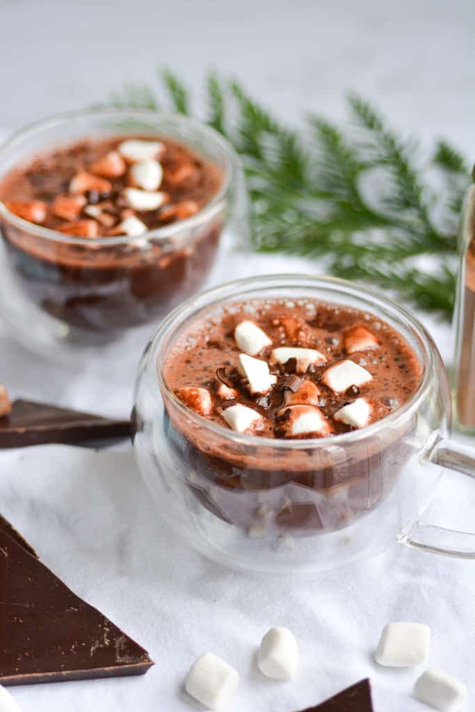 two mugs of vegan gingerbread hot chocolate with marshmallows and shaved chocolate