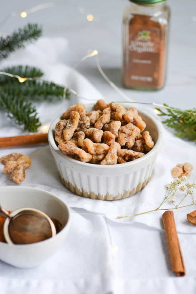 Nuts in a white ramekin on a white napkin with cinnamon sticks and greenery