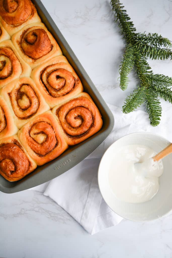 Over head shot of freshly baked cinnamon rolls next to a bowl of frosting