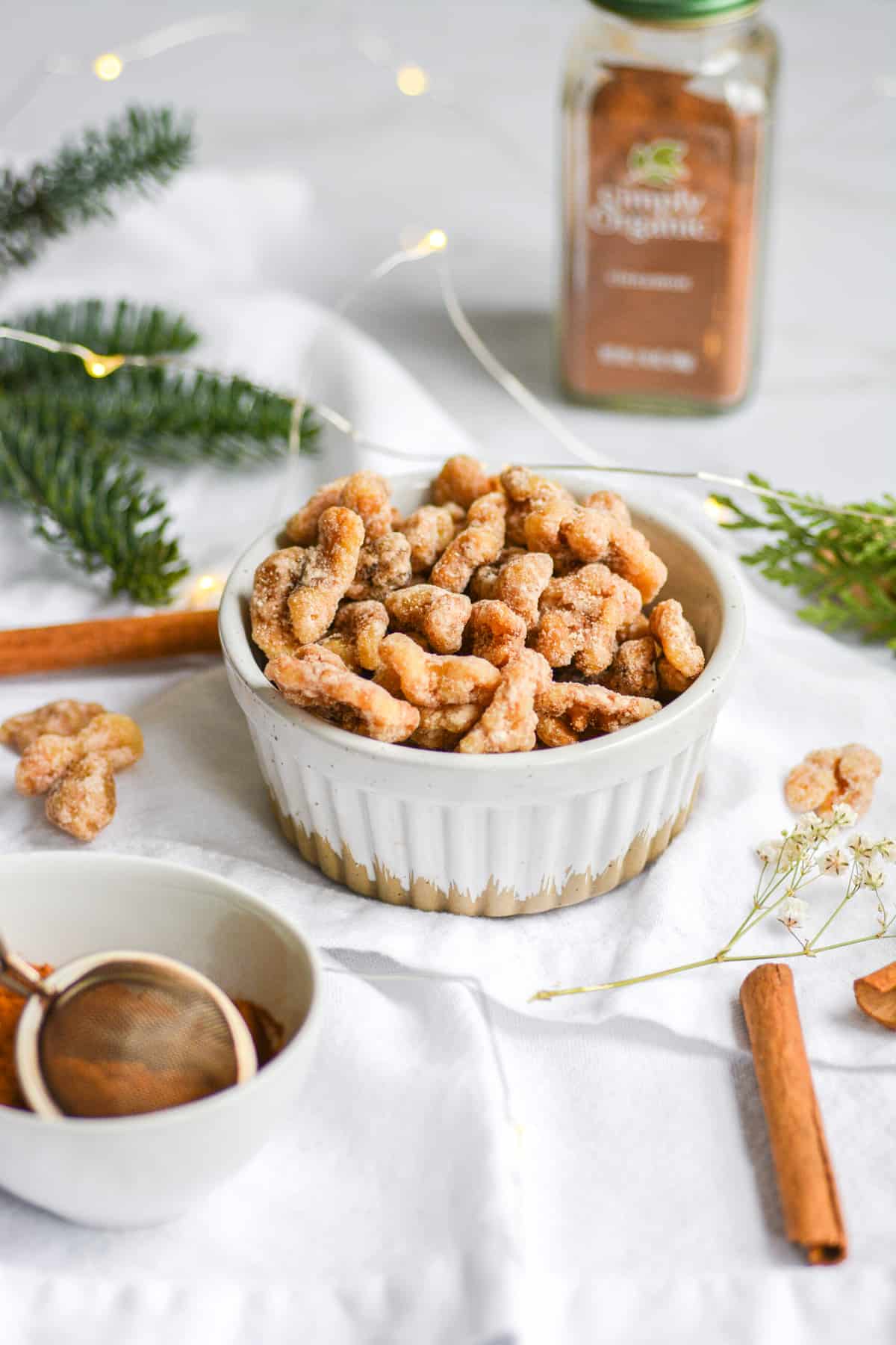 Vegan Cinnamon Sugar Candied Walnuts in a white bowl on a white napkin with cinnamon sticks in the foreground