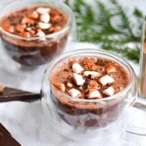 2 mugs of vegan gingerbread hot chocolate topped with marshmallows and shaved chocolate