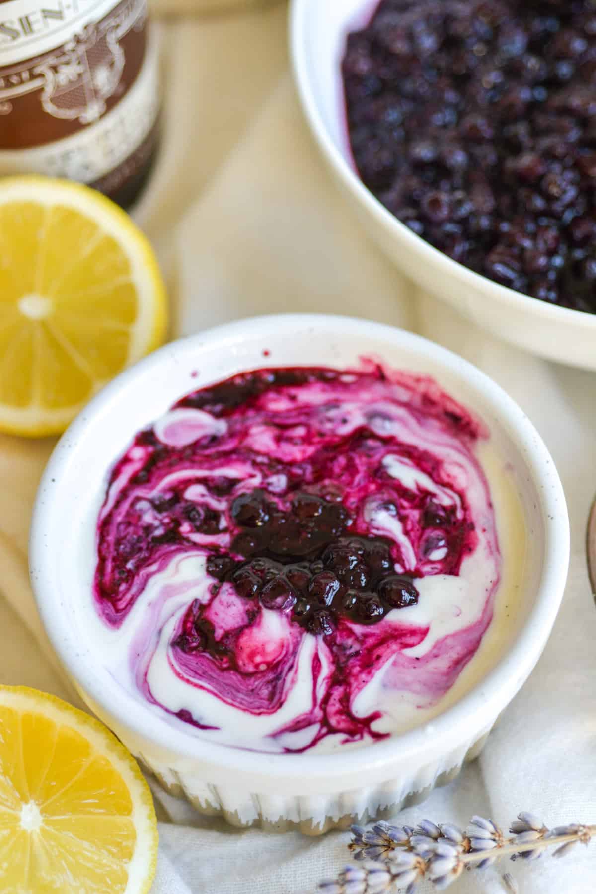 A small ramekin with yogurt in it swirled with blueberry compote.