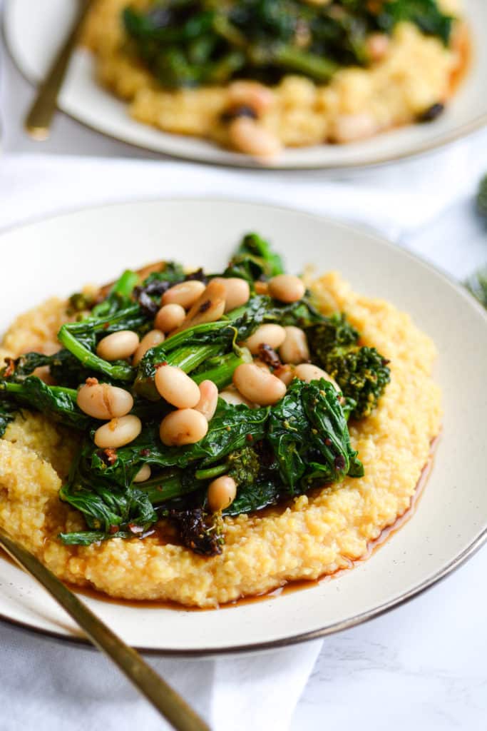 two plates of polenta on a white boars with gold forks