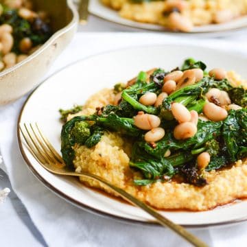 close up of a plate of polenta with broccoli rabe and white beans with a gold fork