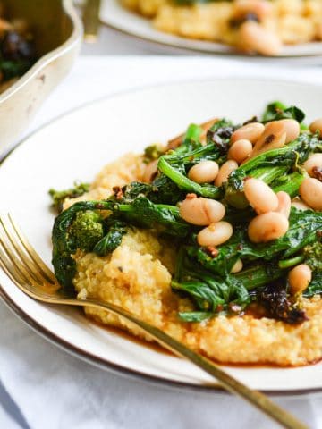 close up of a plate of polenta with broccoli rabe and white beans with a gold fork