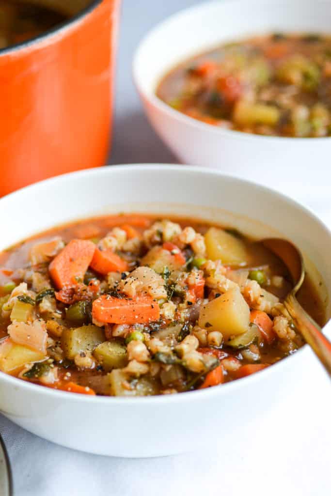 Two bowls of Vegetable and Barley Stew next to an orange dutch oven