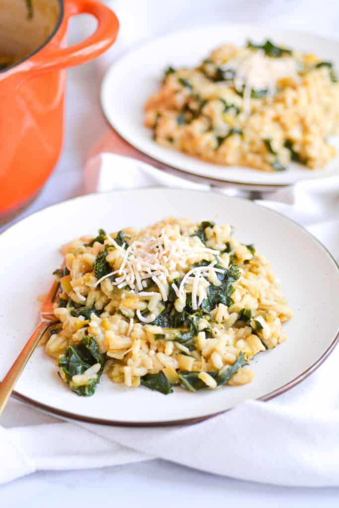 two plates of vegan leek and kale risotto next to an orange dutch oven